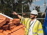 Manlig projektledare iklädd bygghjälm står på taket i en bostadsrättsförening och pekar